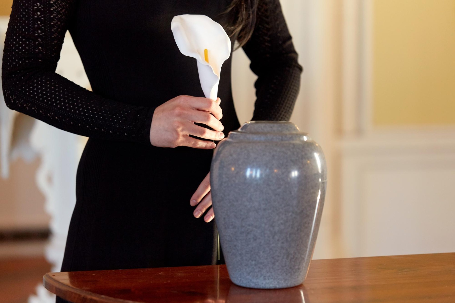 Cremation, people and mourning concept - woman with flowers and cinerary urn at funeral in church